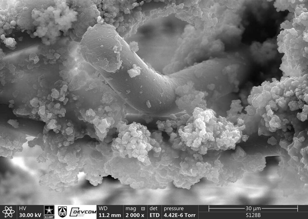 Metal organic framework (MOF) crystals adhered to a nonwoven polymer fiber, under a scanning electron microscope. MOF crystal sizes can be under 1 µm.